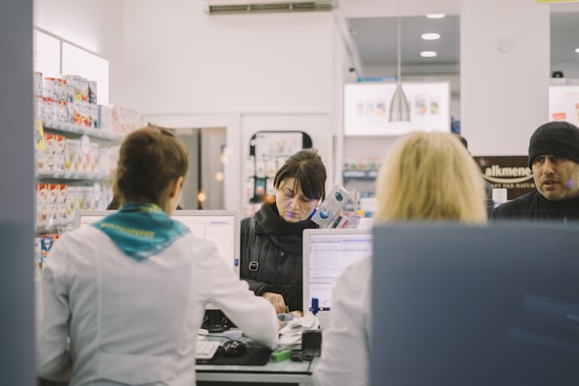 Inside a pharmacy, a man and woman at the check-out counter and two women working.